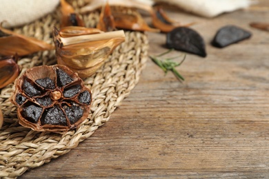 Photo of Wicker mat with black garlic on wooden table, space for text