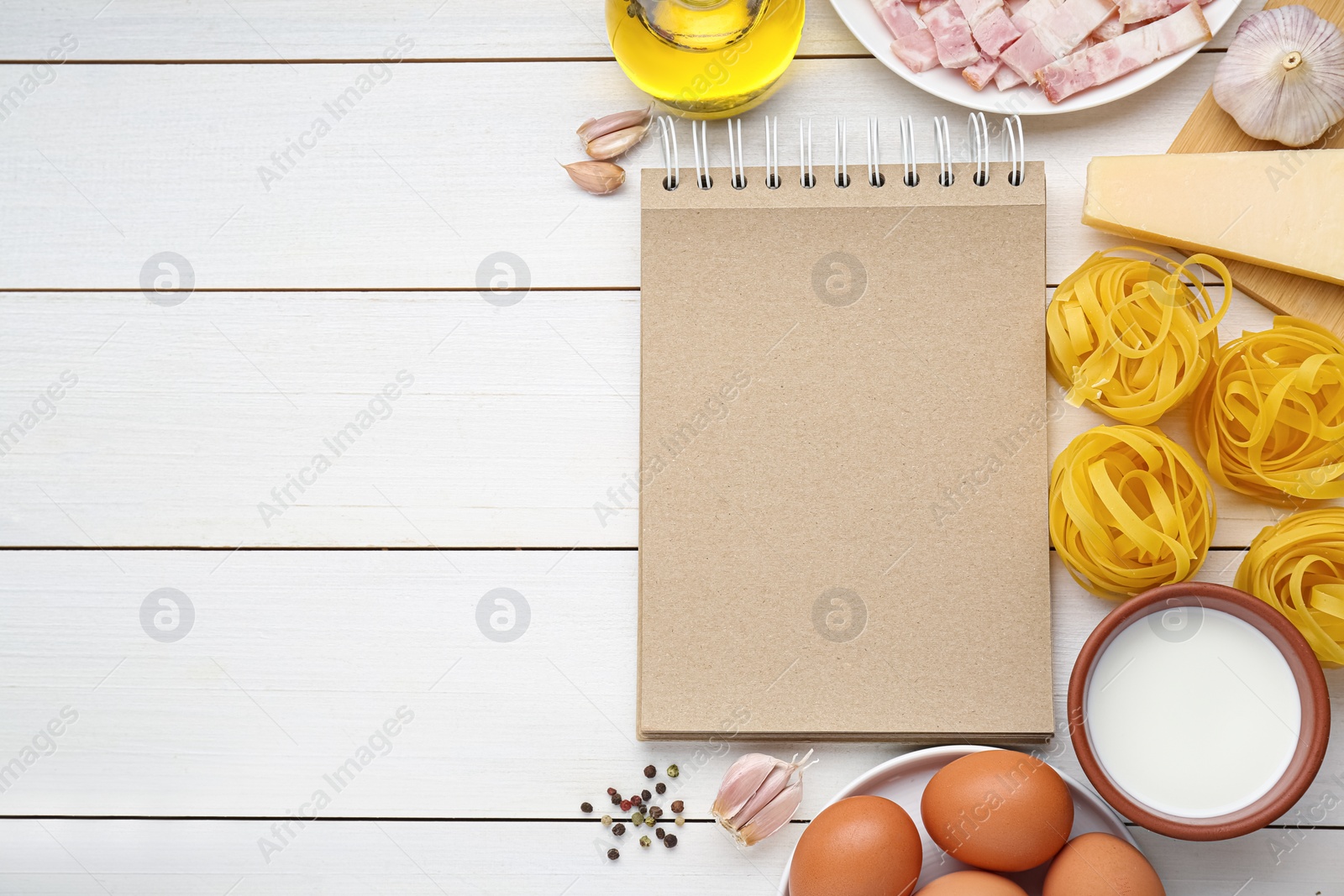 Photo of Blank recipe book and different ingredients on white wooden table, flat lay. Space for text