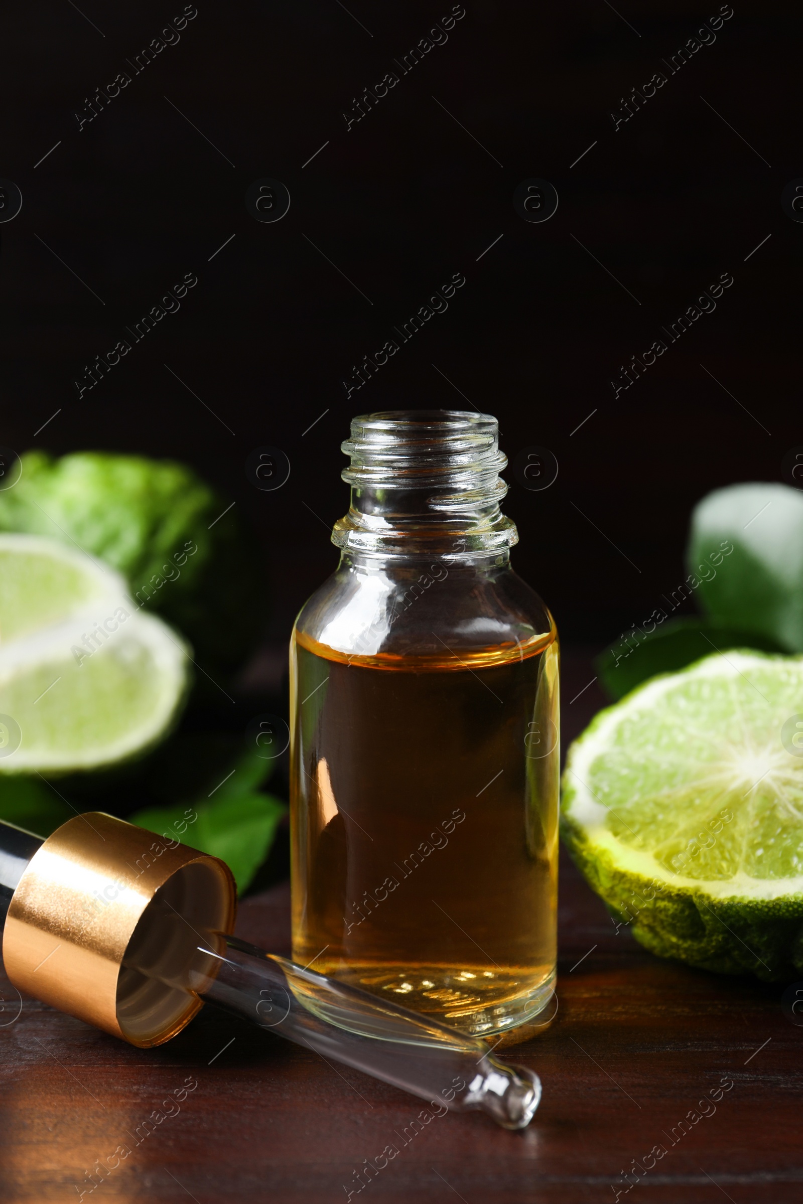 Photo of Bottle of essential oil, pipette and fresh bergamot fruit on wooden table