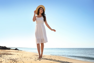 Photo of Happy young woman with hat walking on beach near sea