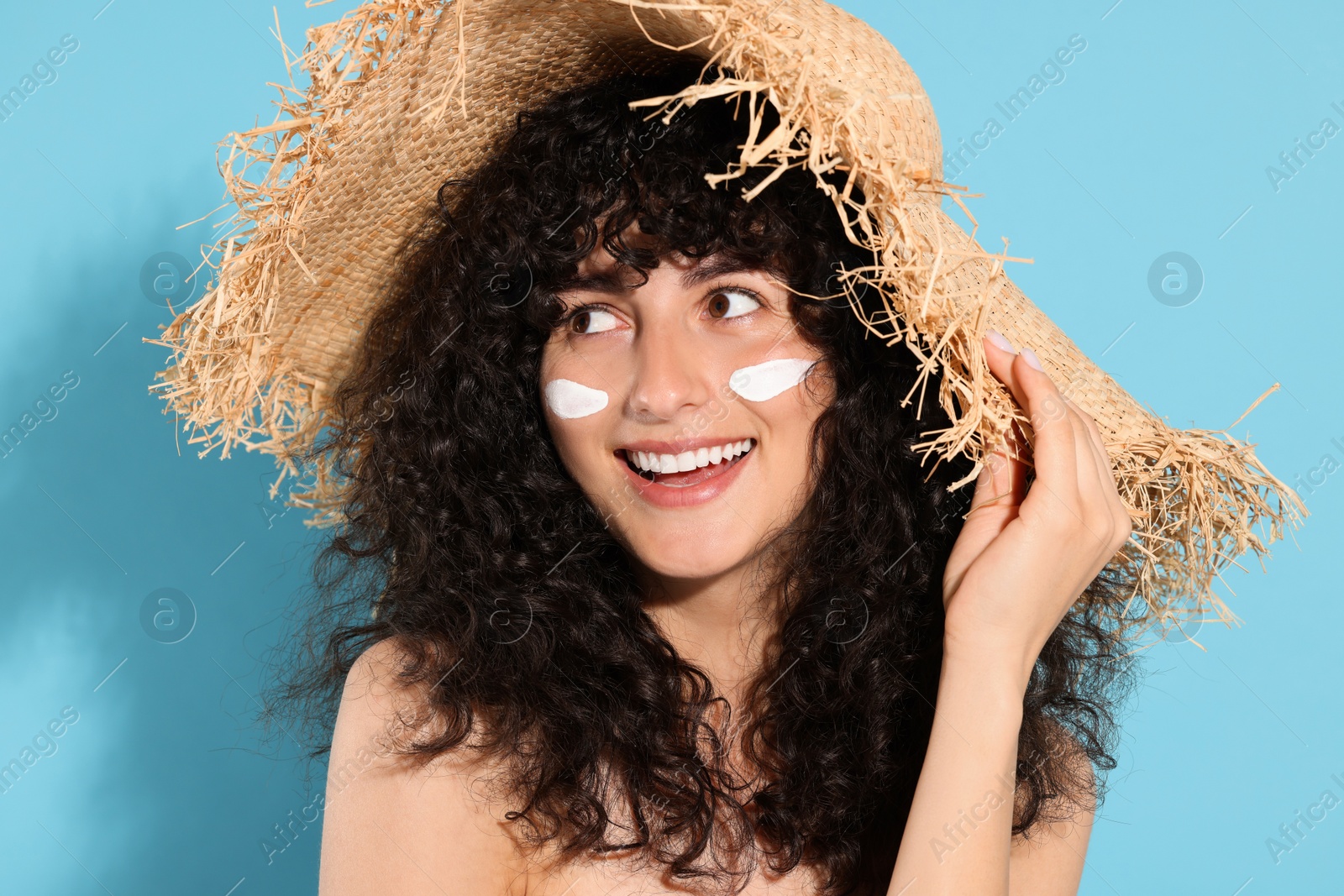 Photo of Beautiful young woman in straw hat with sun protection cream on her face against light blue background