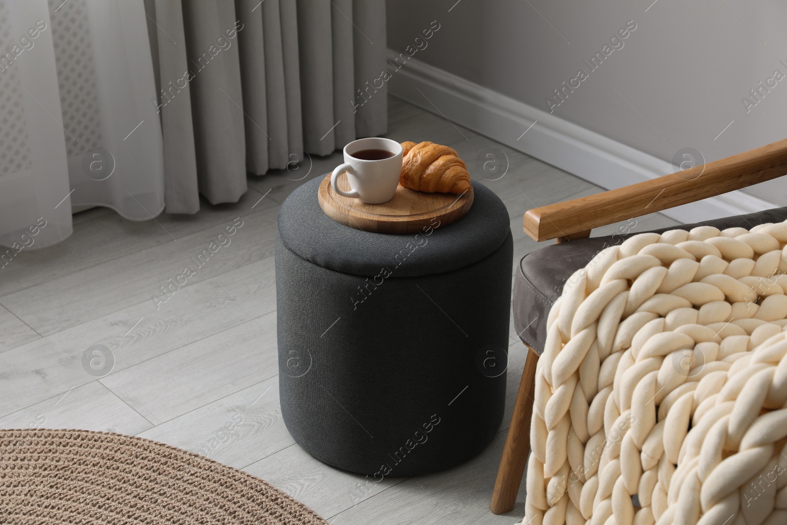 Photo of Tray with cup of tea and croissant on stylish ottoman in room. Interior design