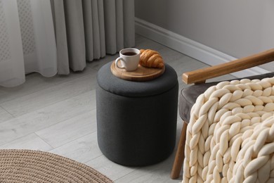 Photo of Tray with cup of tea and croissant on stylish ottoman in room. Interior design