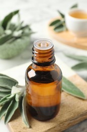 Photo of Bottle of essential sage oil and leaves on white table, closeup