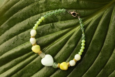 Photo of Beautiful bracelet with gemstones on green leaf, top view