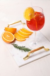 Photo of Glass of tasty Aperol spritz cocktail with orange slices and rosemary on white table