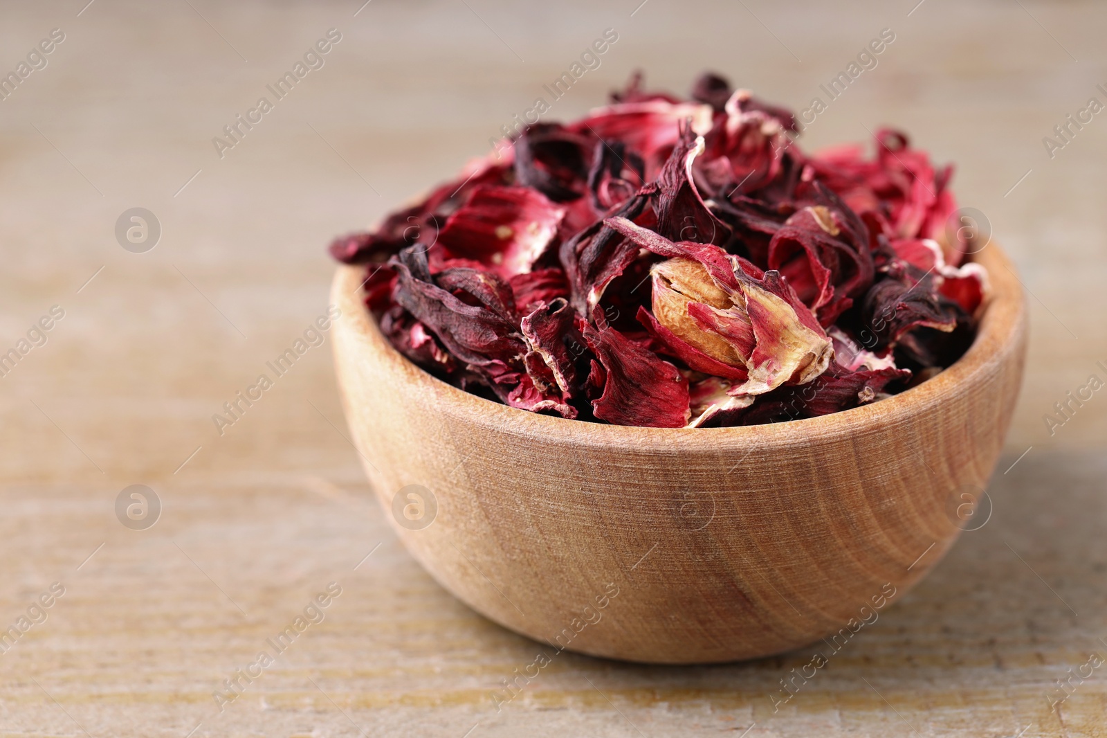 Photo of Dry hibiscus tea in bowl on wooden table, closeup