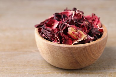 Photo of Dry hibiscus tea in bowl on wooden table, closeup