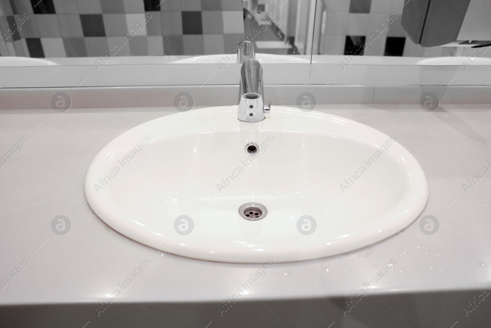 Photo of Clean ceramic sink near tiled wall in public toilet