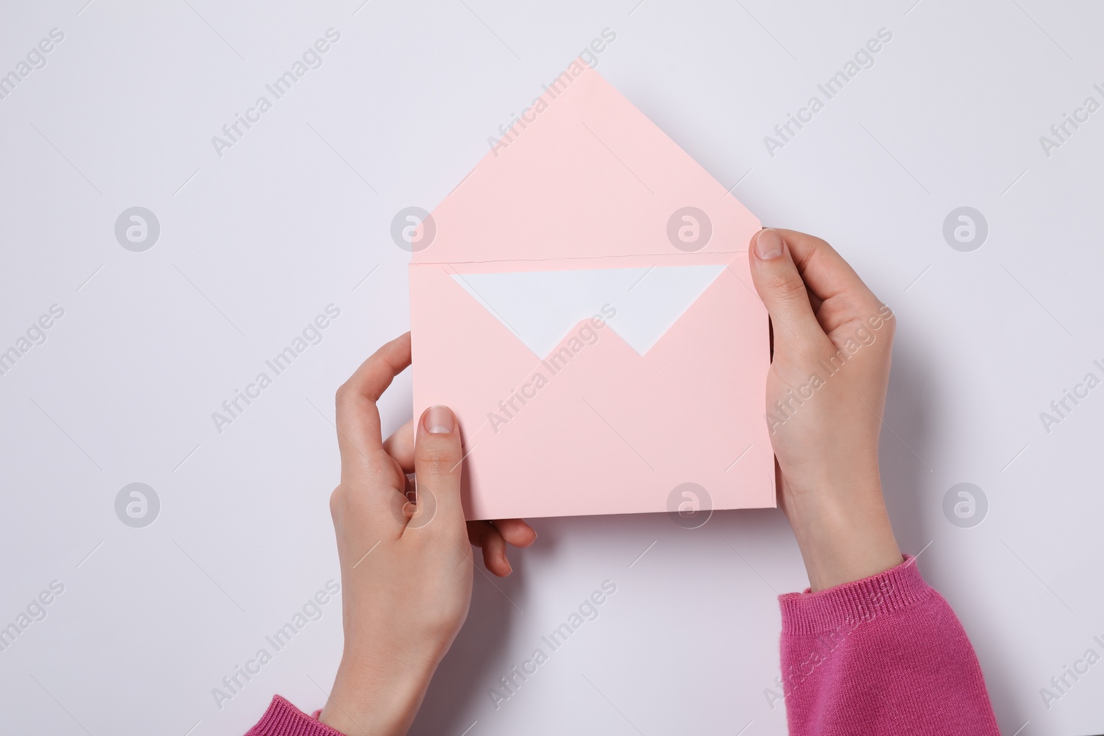 Photo of Woman holding letter envelope with card at white table, top view