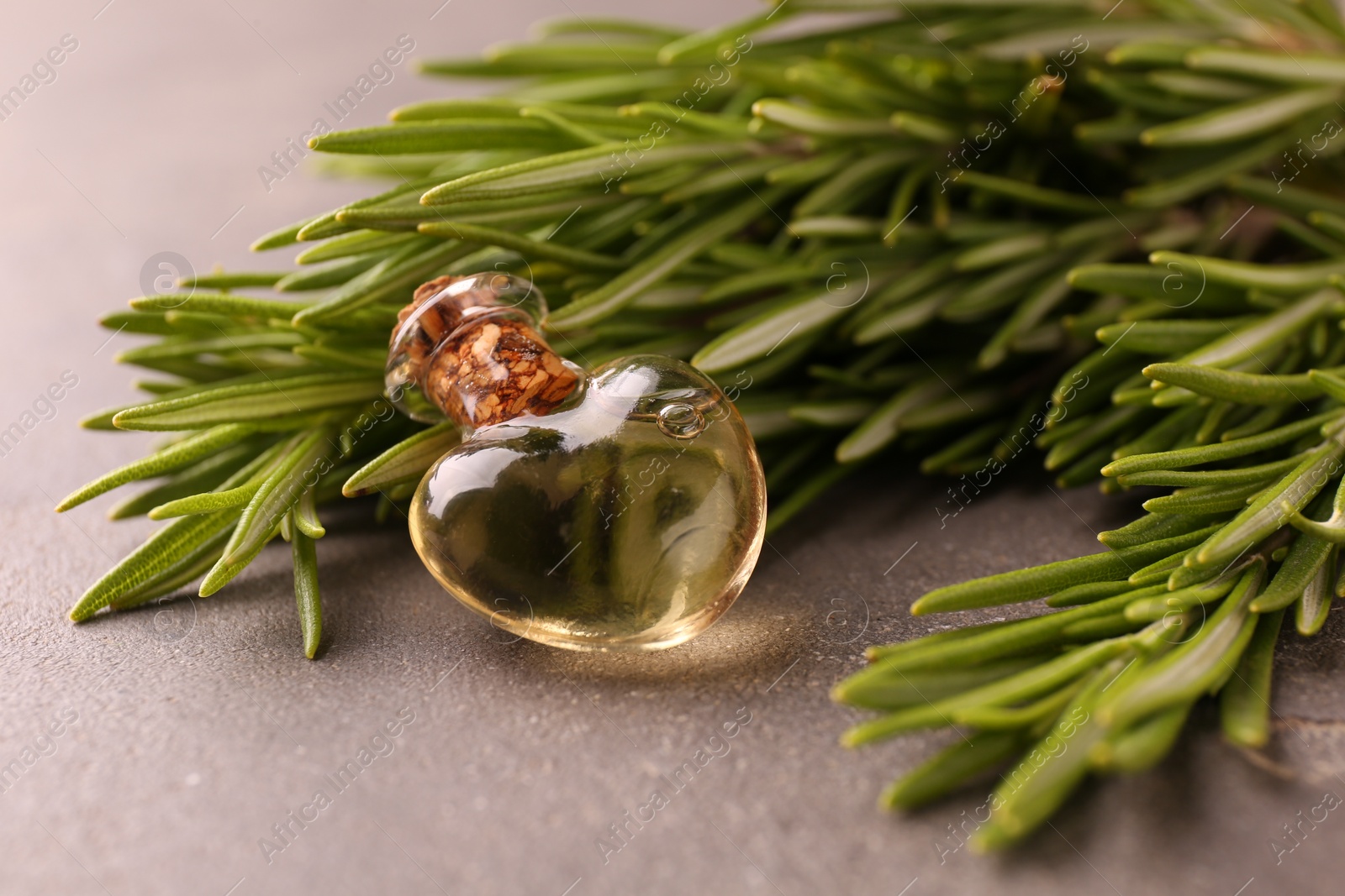 Photo of Essential oil in bottle and rosemary on grey table, closeup