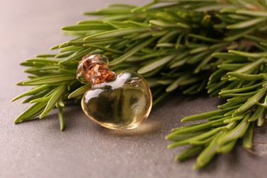 Essential oil in bottle and rosemary on grey table, closeup