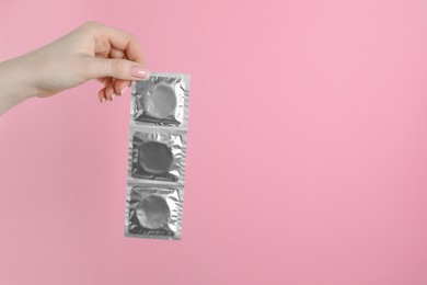 Photo of Woman holding condoms on pink background, closeup. Space for text