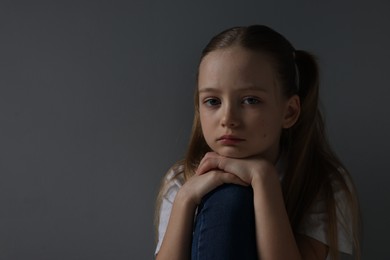 Photo of Sad girl sitting near dark grey background, space for text