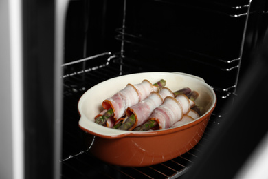 Photo of Uncooked bacon wrapped asparagus in baking dish on oven rack, closeup