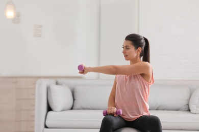 Young woman in fitness clothes doing exercise with dumbbells at home. Space for text