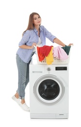 Young woman holding basket with dirty laundry near washing machine on white background