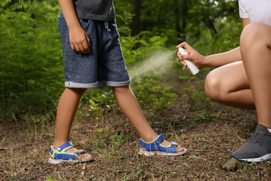 Photo of Woman applying insect repellent on her son's leg in park, closeup. Tick bites prevention