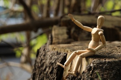 Photo of Wooden human figure sitting on stump outdoors, space for text