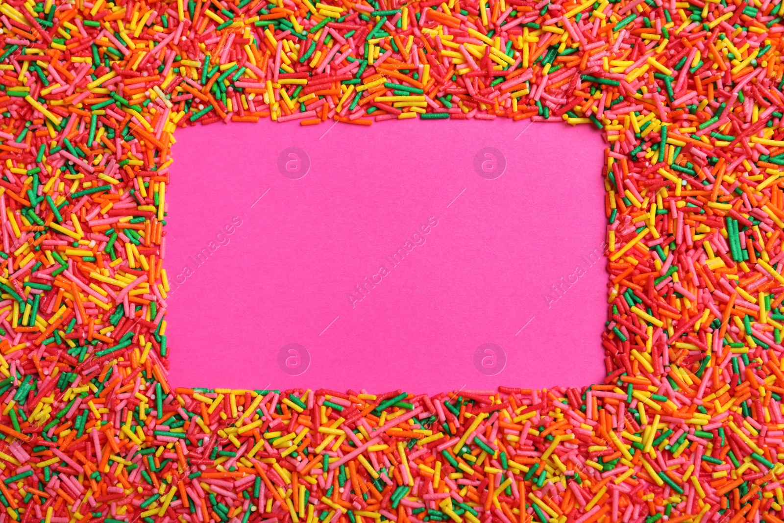 Photo of Frame of bright colorful sprinkles on pink background, flat lay with space for text. Confectionery decor