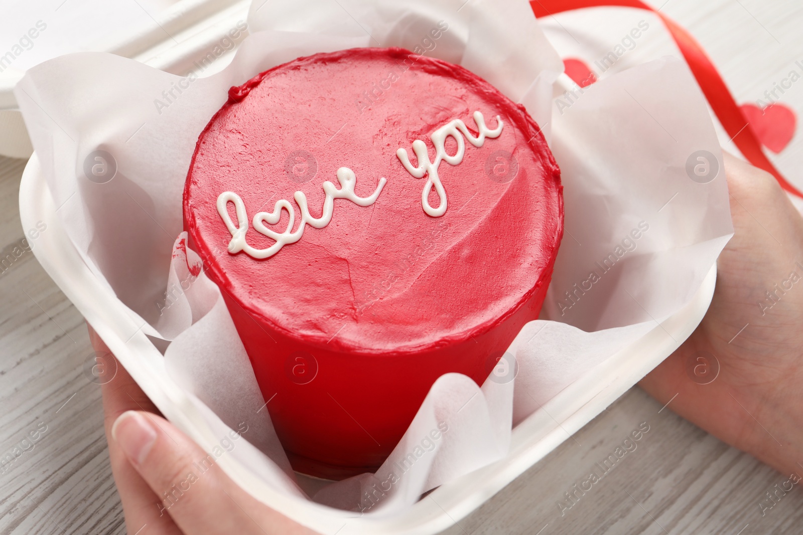 Photo of Woman holding takeaway box with bento cake at white wooden table, closeup. St. Valentine's day surprise