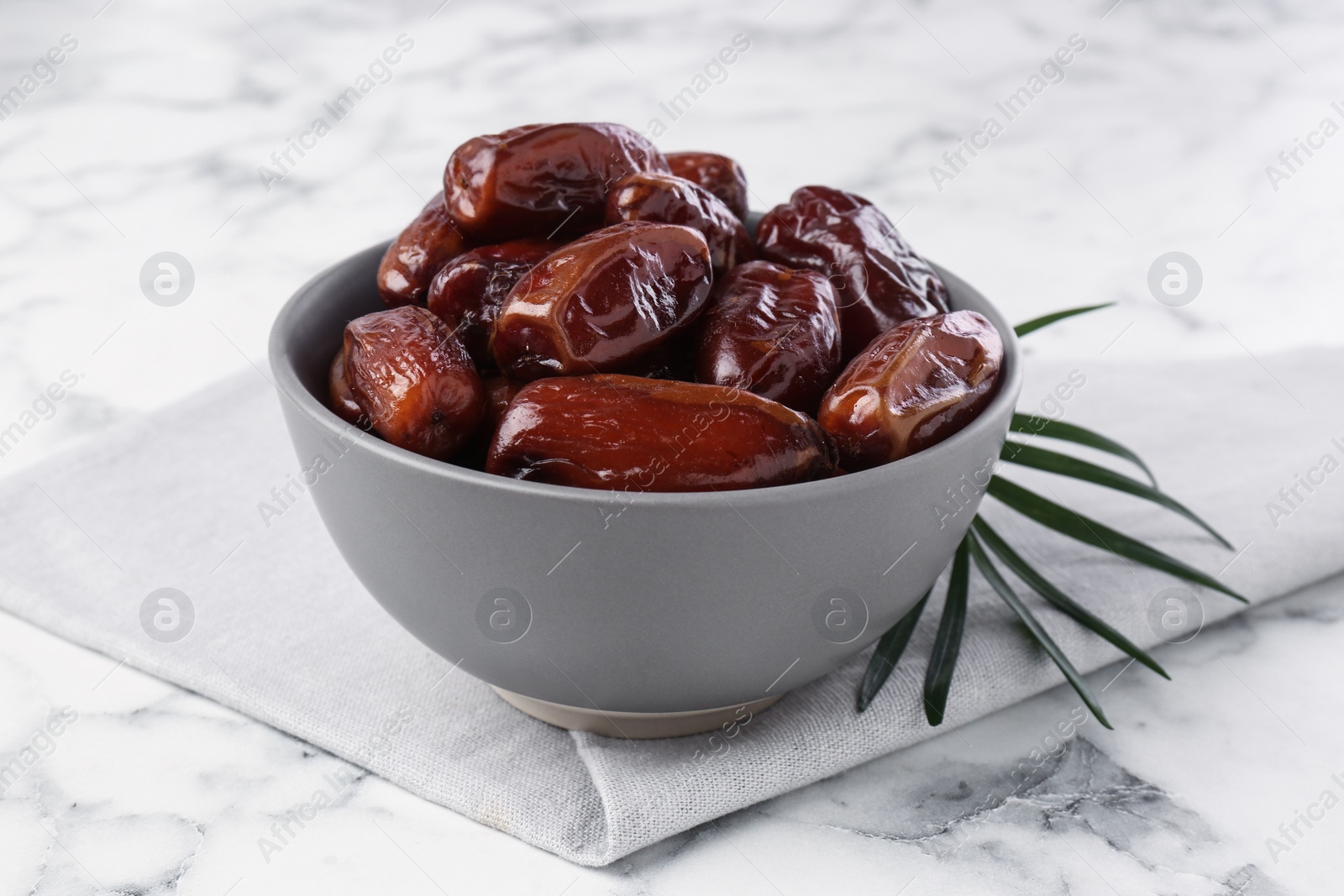 Photo of Sweet dried dates in bowl on white marble table, closeup