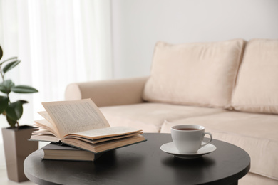 Photo of Books and cup of tea on table near modern sofa indoors. Home interior