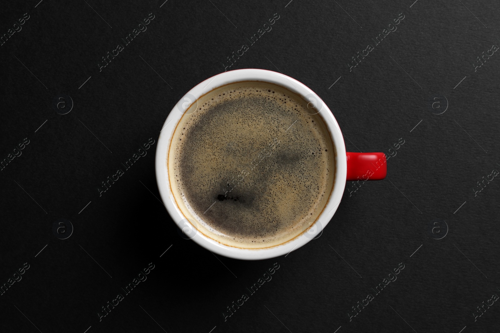 Photo of Ceramic cup with hot aromatic coffee on black background, top view