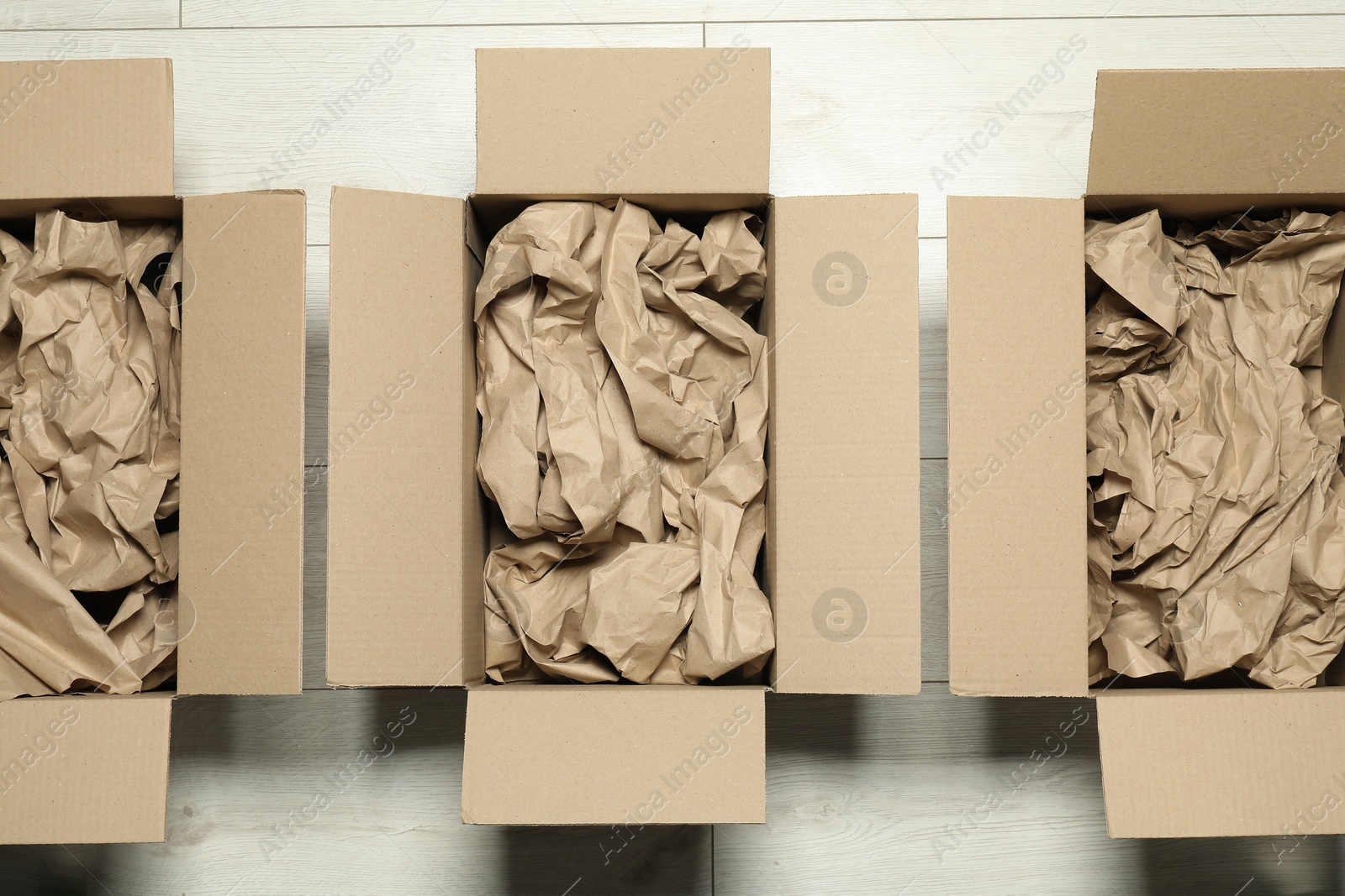 Photo of Open cardboard boxes with crumpled paper on white wooden floor, flat lay