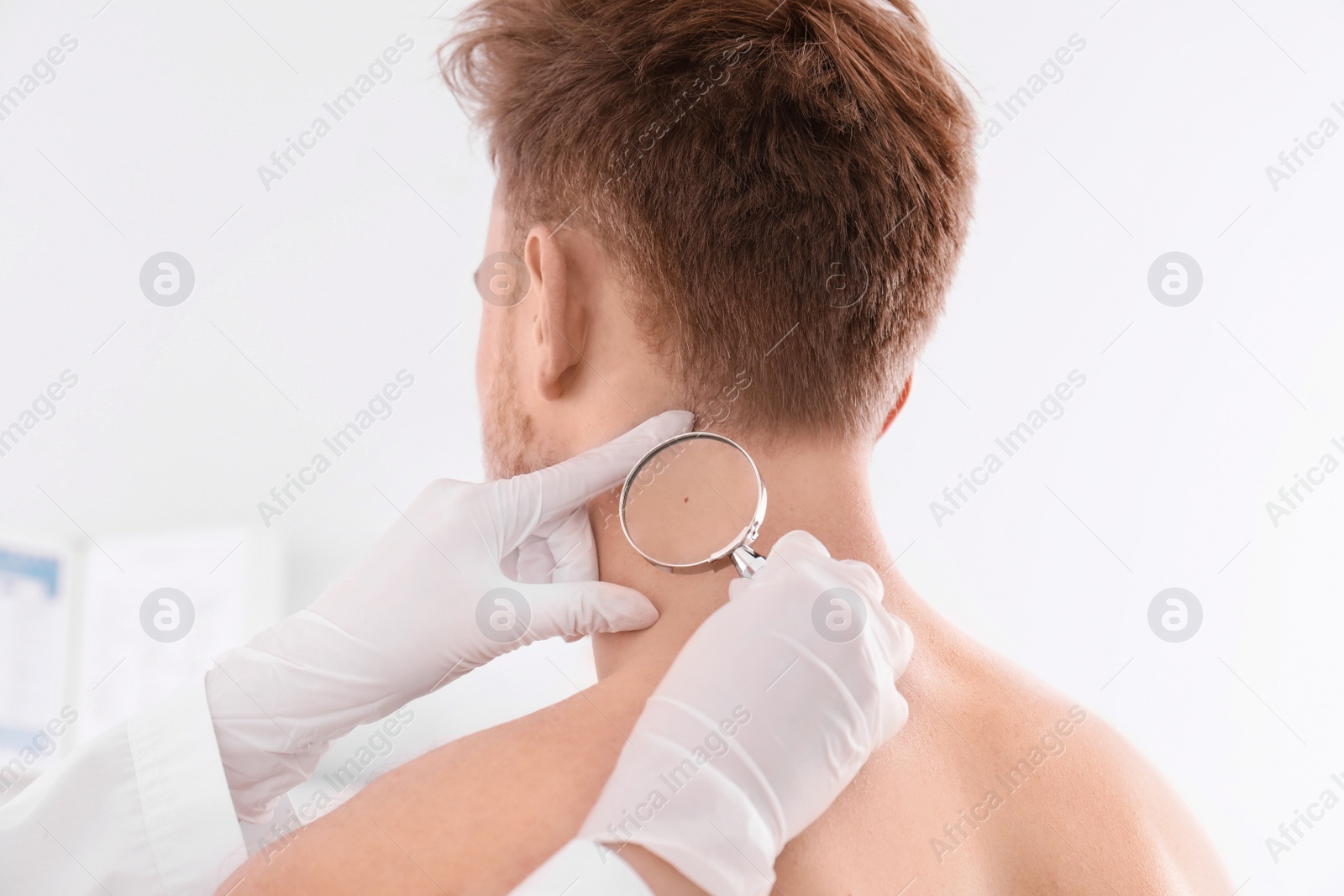 Photo of Dermatologist examining patient with magnifying glass in clinic, closeup view