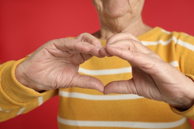 Photo of Elderly woman making heart with her hands on red background, closeup