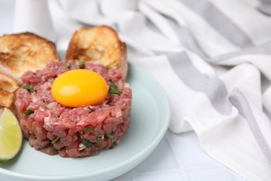 Photo of Tasty beef steak tartare served with yolk, toasted bread and lime on white tiled table, closeup. Space for text