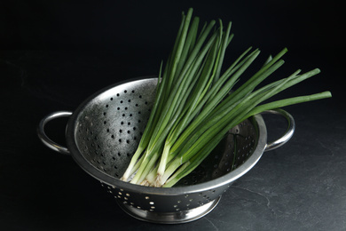 Photo of Fresh green spring onions in colander on black table