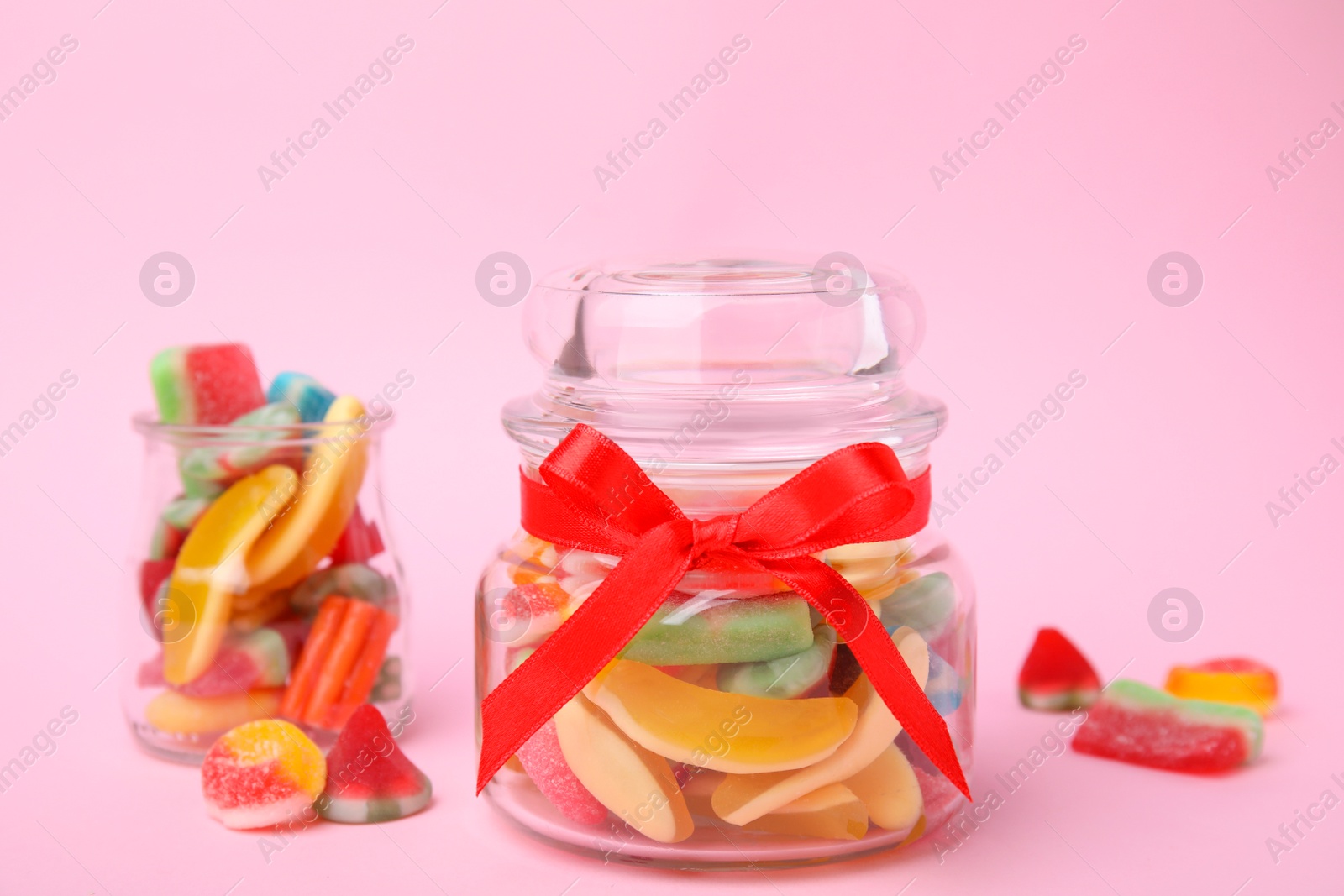 Photo of Glass jars with tasty colorful jelly candies on pink background