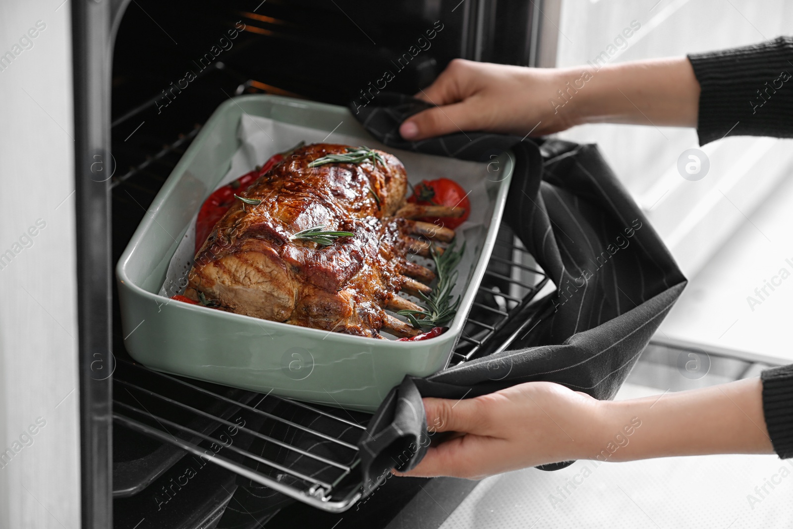 Photo of Woman taking delicious ribs out of oven, closeup