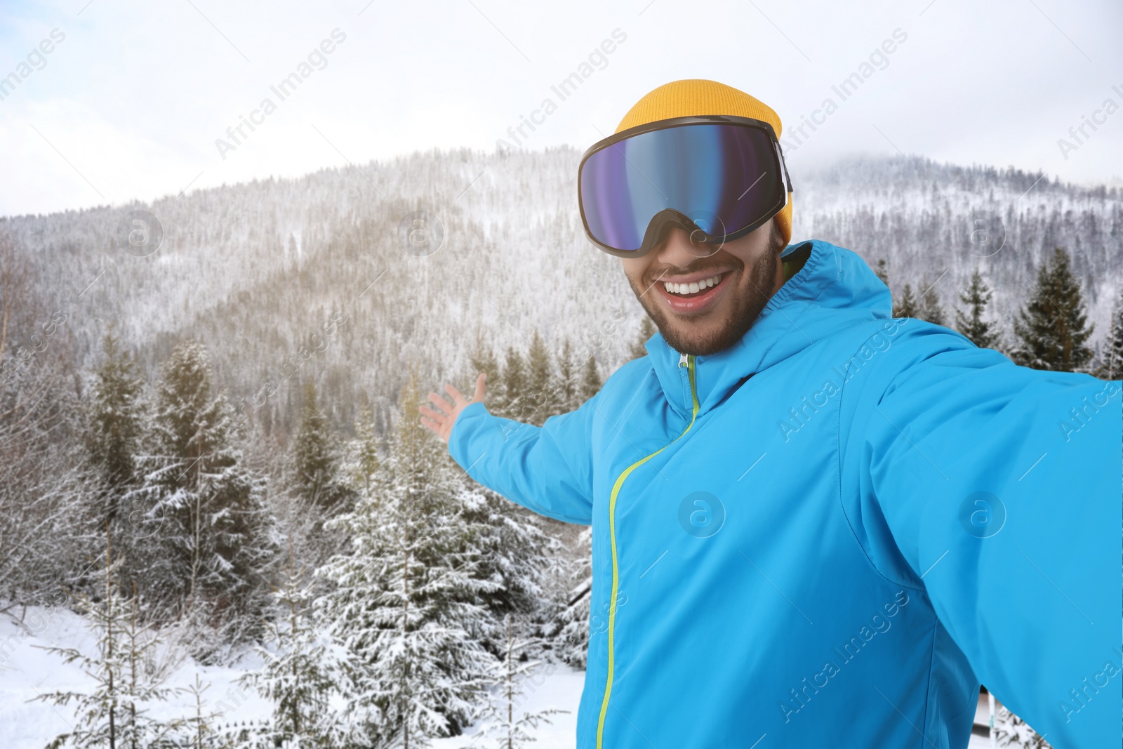 Image of Smiling young man in ski goggles taking selfie in snowy mountains