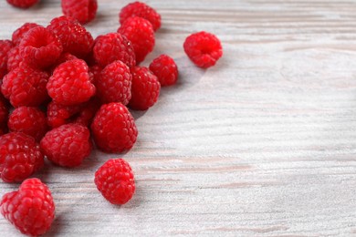 Photo of Tasty ripe raspberries on white wooden table, space for text