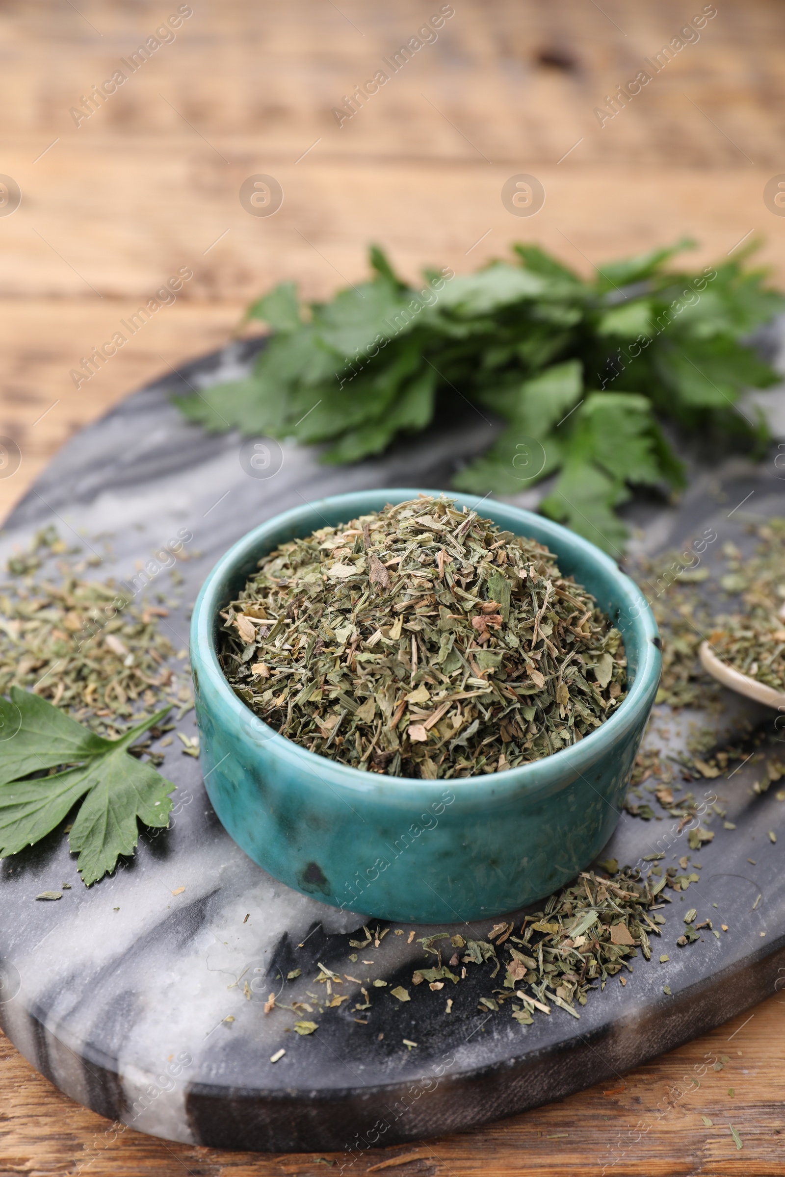 Photo of Dried parsley in bowl on wooden table, closeup. Space for text