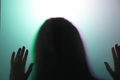 Photo of Silhouette of creepy ghost behind glass against color background