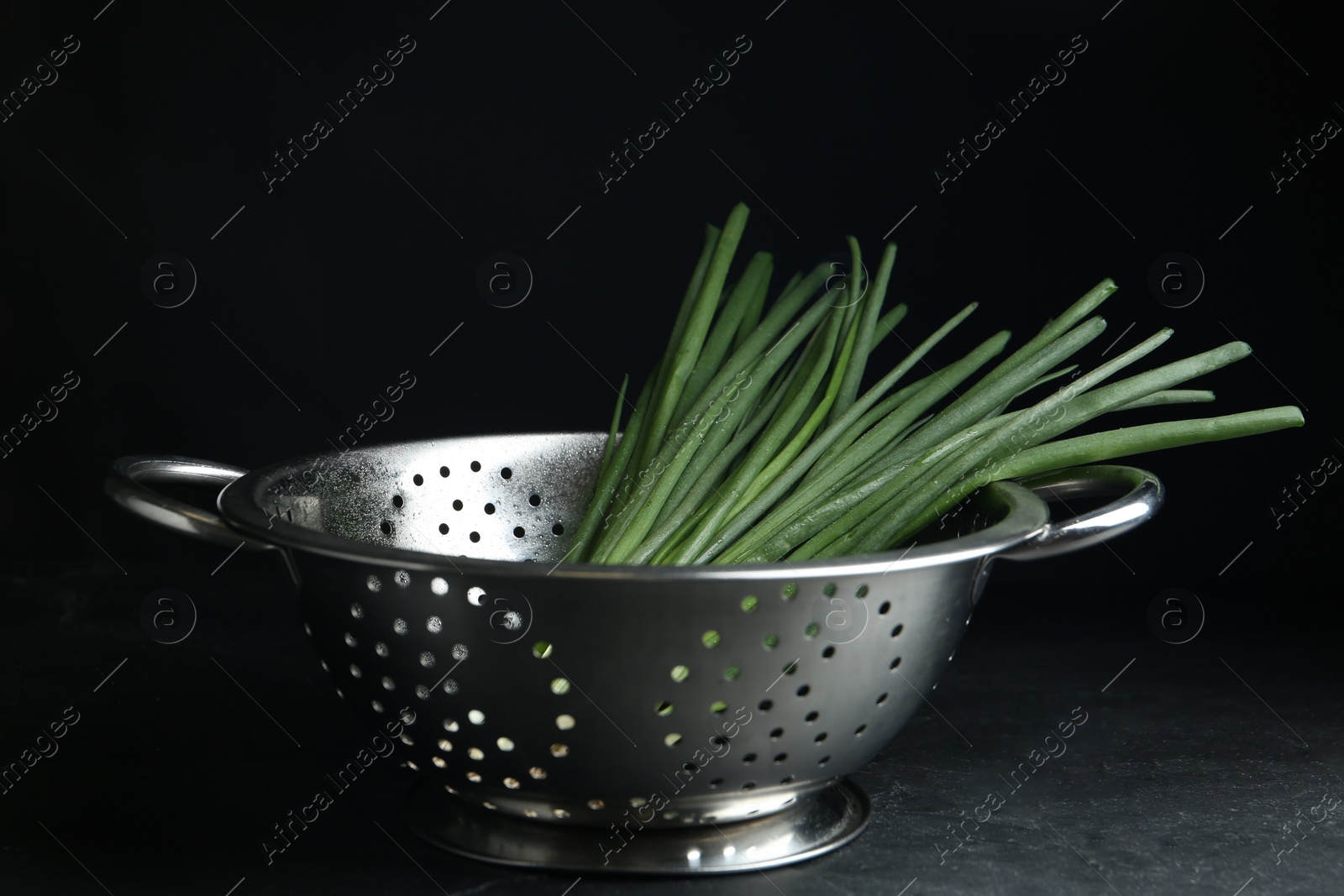 Photo of Fresh green spring onions in colander on black table