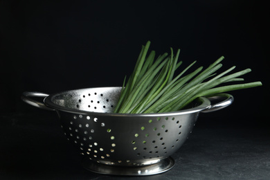 Fresh green spring onions in colander on black table