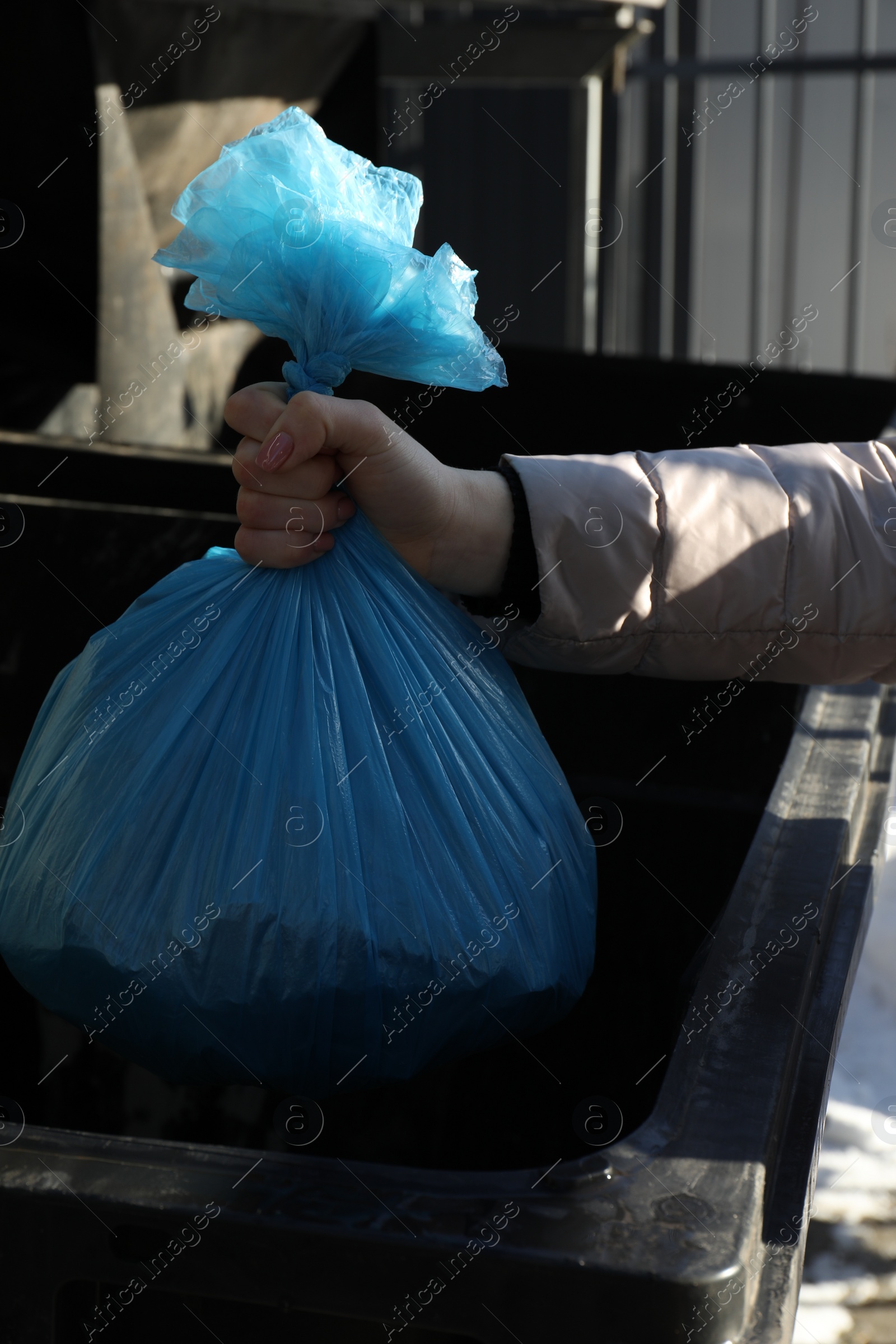 Photo of Woman throwing trash bag full of garbage in bin outdoors, closeup