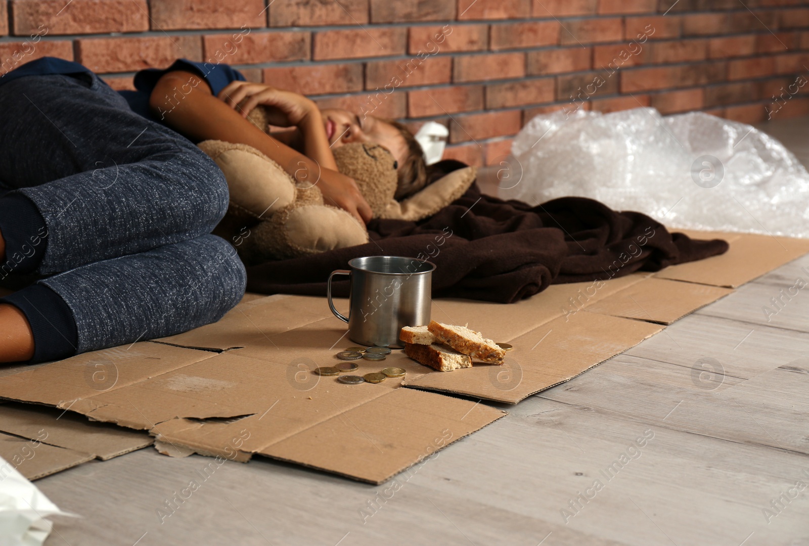 Photo of Poor homeless boy sleeping with his toy on floor near brick wall