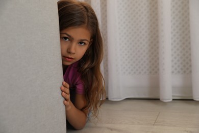 Photo of Sad little girl hiding behind sofa at home. Domestic violence concept