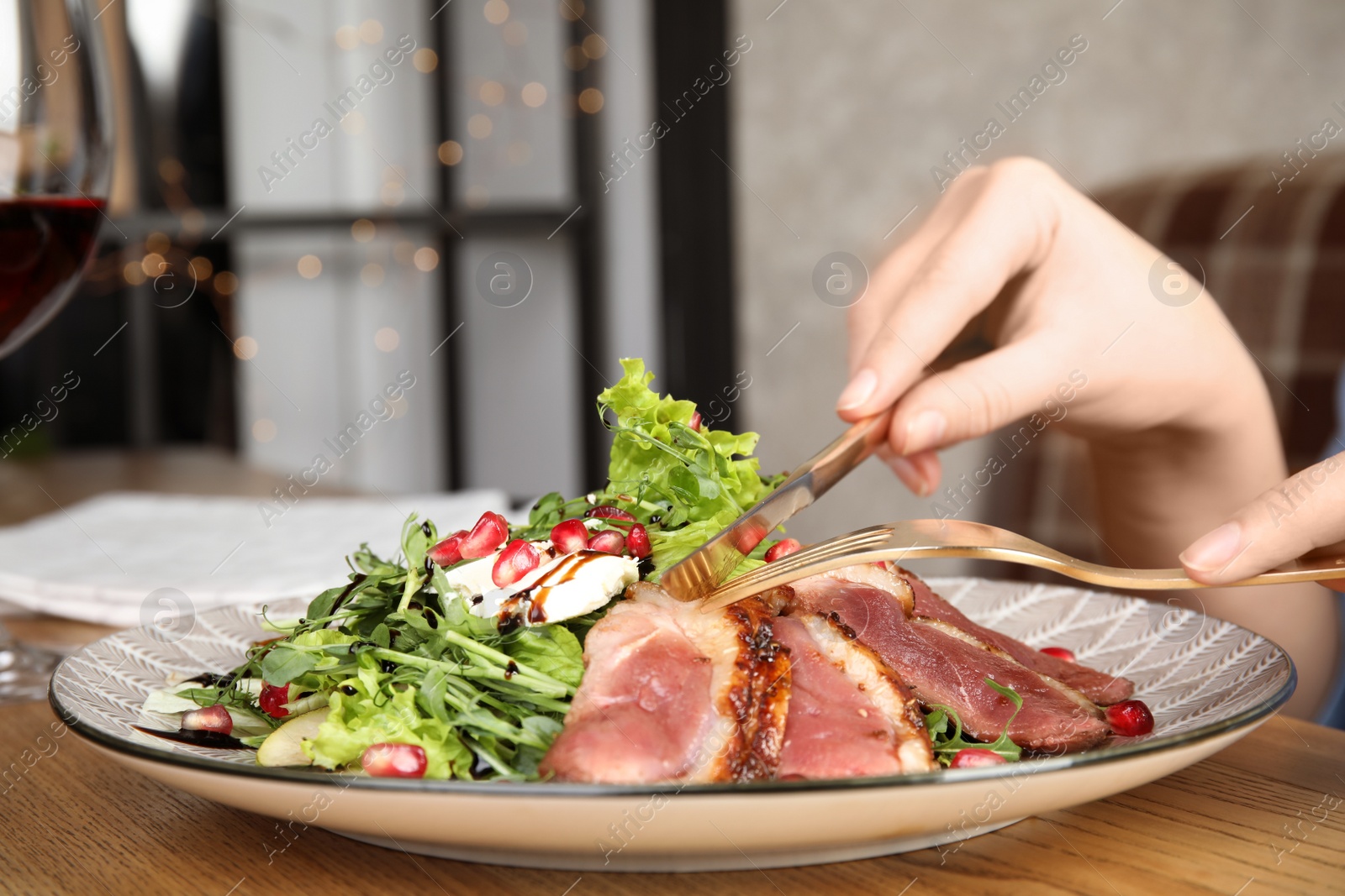 Photo of Woman eating delicious salad with roasted duck breast at wooden table, closeup