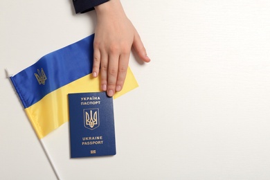 Woman with Ukrainian travel passport, flag and space for text on light background, top view. International relationships