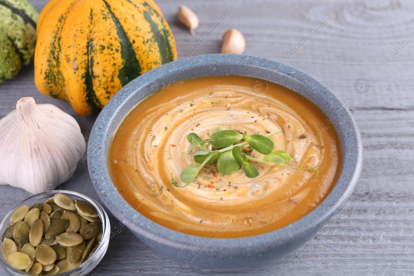 Photo of Tasty pumpkin soup with microgreens in bowl on grey wooden table