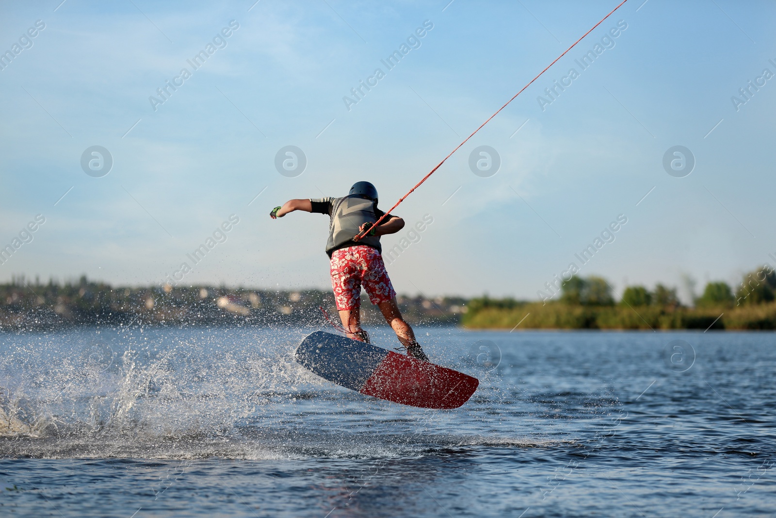 Photo of Teenage wakeboard doing trick on river, back view. Extreme water sport