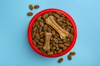 Photo of Dry dog food and treats (chew bones) on light blue background, flat lay