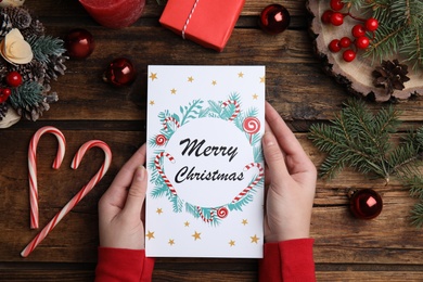 Woman holding Christmas card at wooden table, top view